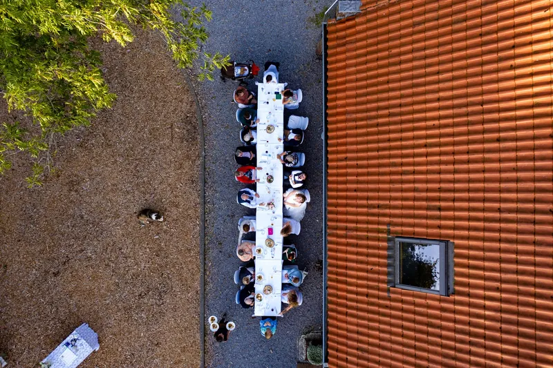Dronefoto recht van boven op een lange bruiloftstafel met gasten naast een houten gevel
