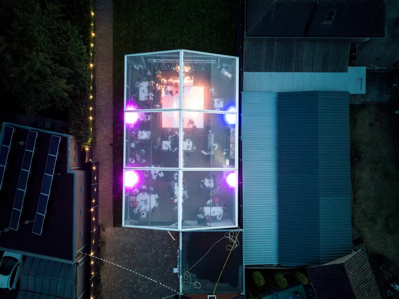 Dronefoto bij nacht van een verlichte glazen toren op het erf van een bruiloftsfeest