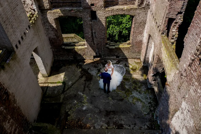 Dronefoto van een bruidspaar tussen de muren van een kasteelruïne