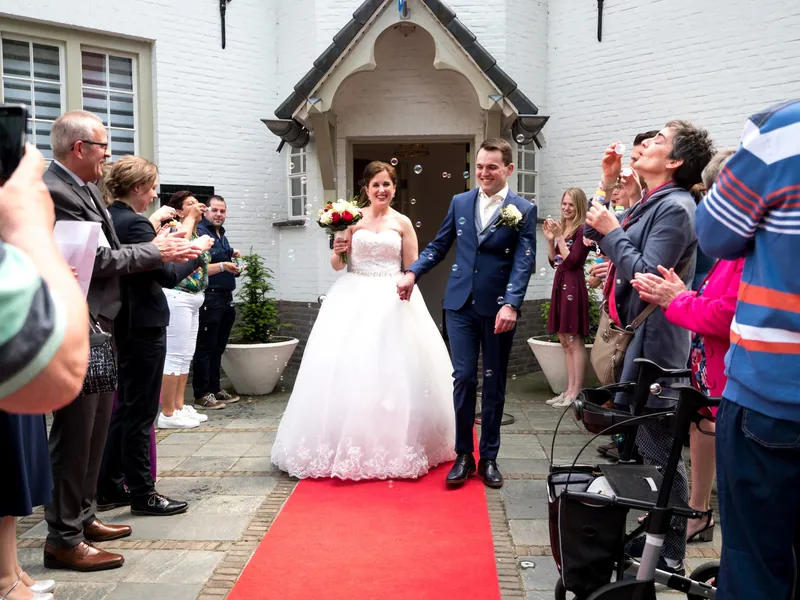 Bruidspaar loopt hand in hand over een rode loper tussen applaudisserende gasten