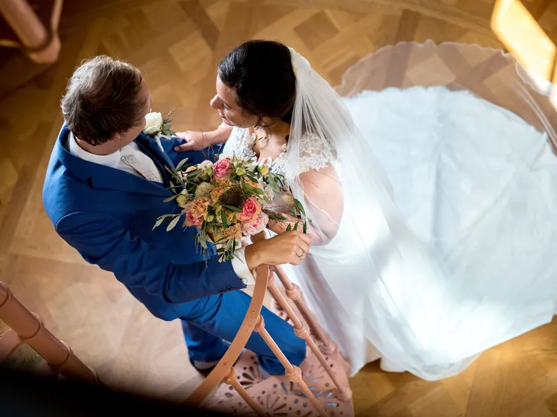 Bruidspaar van bovenaf gefotografeerd, de bruidsjurk waaiert uit over de houten vloer