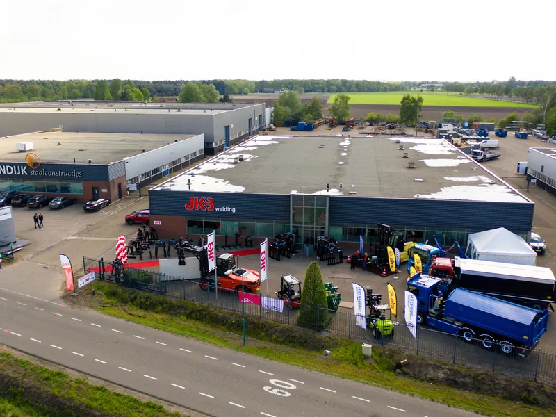 Dronefoto van een bedrijfspand met voertuigen en vlaggen tijdens een open dag