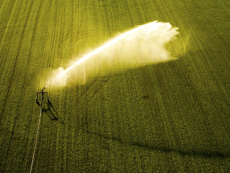 Dronefoto van een beregeningsinstallatie die een veld besproeit in het avondlicht