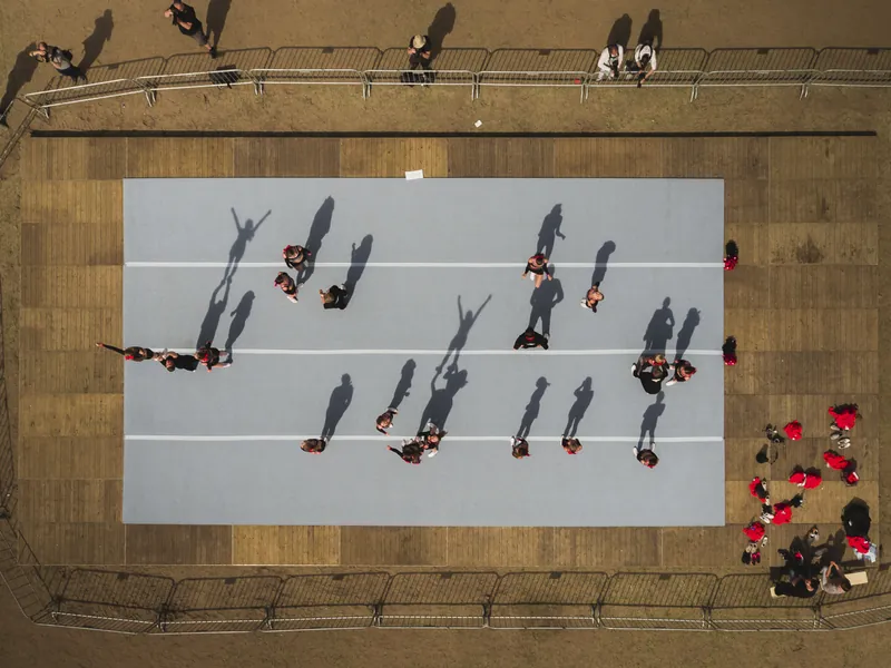 Dronefoto recht van boven op een podium met dansers en lange schaduwen