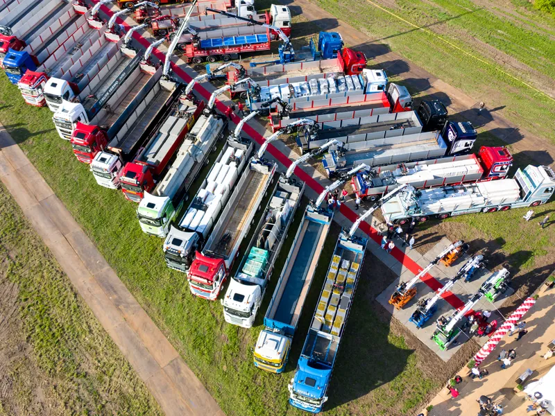 Dronefoto van een lange rij vrachtwagens met laadkranen langs een grasveld
