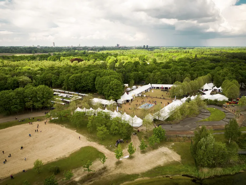 Dronefoto van een evenementterrein met witte tenten in het groen