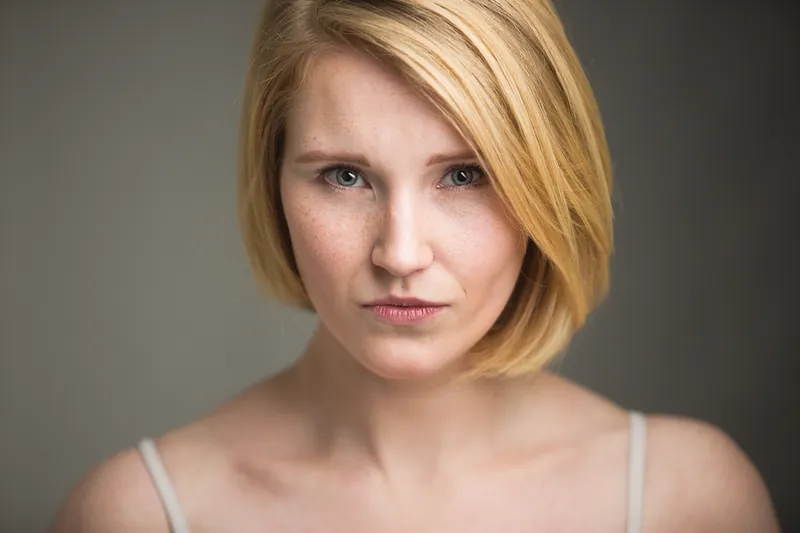 Close-up portret van een vrouw met blond haar en sproeten tegen een grijze achtergrond