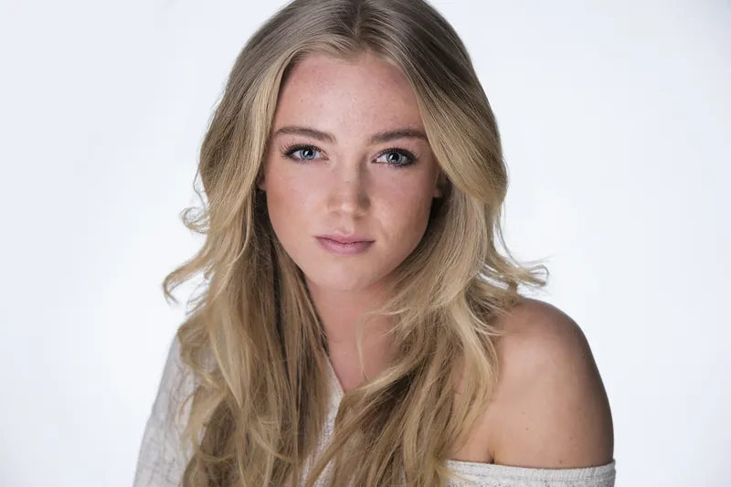 Portret van een jonge vrouw met blond haar tegen een lichte achtergrond
