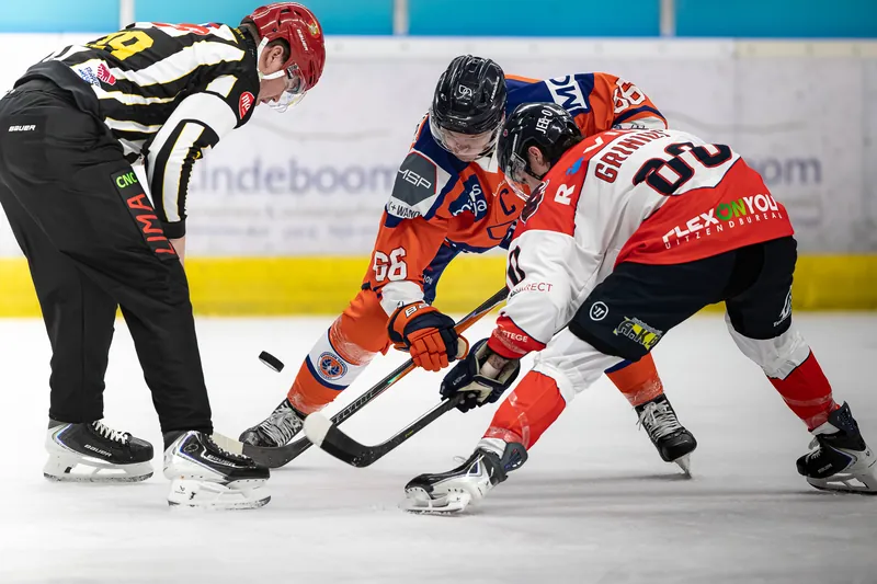 IJshockeyspelers strijden om de puck bij een bully, de scheidsrechter staat ernaast