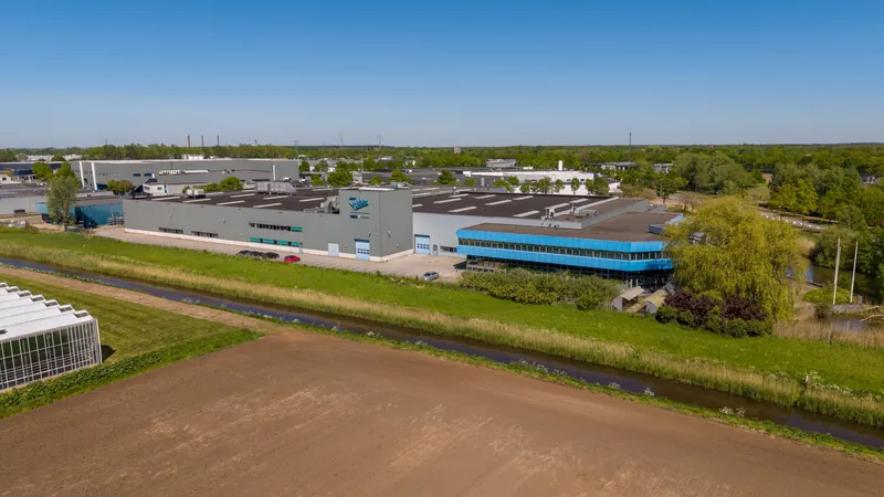 Dronefoto van een bedrijfsgebouw langs een sloot met open landschap