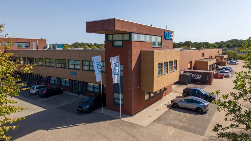 Dronefoto van een bedrijfspand met baksteentoren en vlaggen op een bedrijventerrein