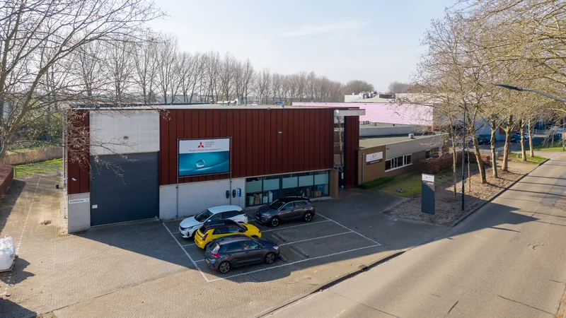 Dronefoto van een bedrijfspand met rode gevel en parkeerplaats op een bedrijventerrein