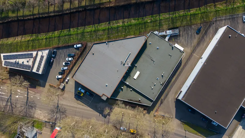 Dronefoto schuin van boven op bedrijfsdaken met zonnepanelen