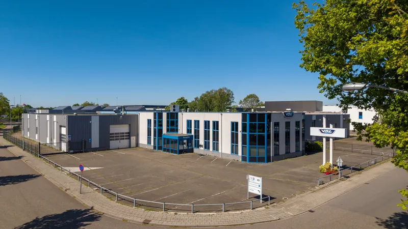 Dronefoto van een bedrijfspand met kantoorgedeelte onder een strakblauwe lucht