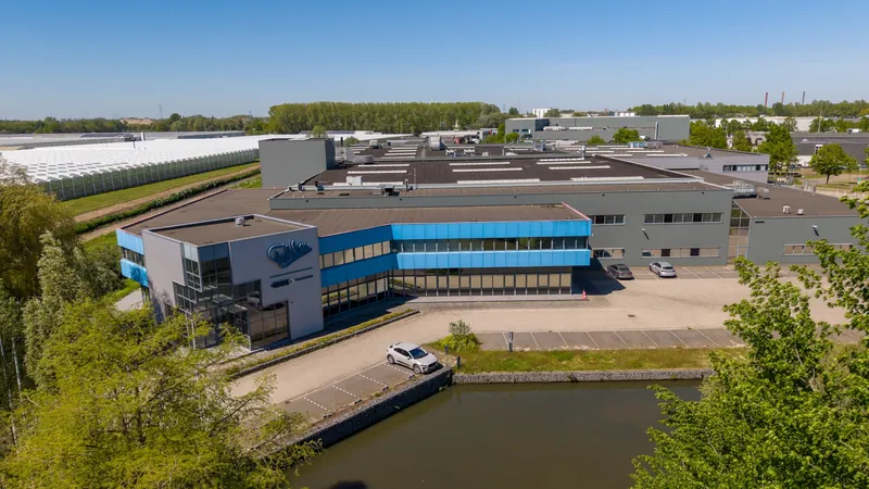 Dronefoto van een productiehal aan het water met kantoorvleugel in blauwe tinten