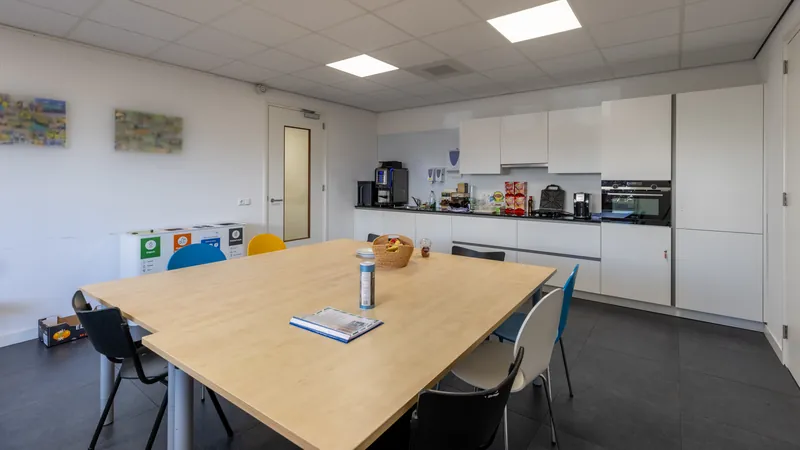 Interieur van een lichte bedrijfskantine met keuken en grote tafel